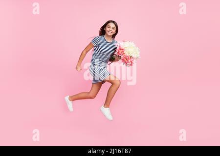 Foto von glänzenden süßen Mädchen gekleidet gestreiftes Kleid hält Haufen springen hoch läuft isoliert rosa Farbe Hintergrund Stockfoto