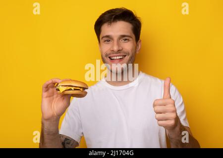 Funny Guy Holding Burger Zeigt Daumen Nach Oben Stockfoto