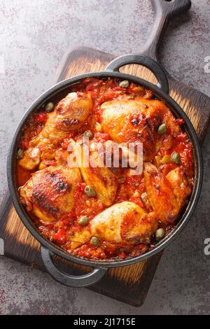 Mediterranes Huhn mit Tomaten, Paprika, Zwiebeln und Knoblauch in einer Pfanne auf dem Tisch gebacken. Vertikale Draufsicht von oben Stockfoto