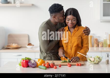 Loving Schwarz Mann Küssen Frau Während Sie Kochen Lebensmittel In Küche Innenraum Stockfoto