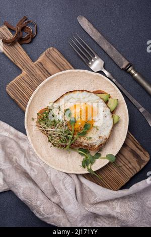 Blick von oben auf Sandwich mit Spiegelei, Toast, Avocado, Luzerne und grünen Erbsensprossen mikrogrün zum Frühstück auf schwarzem Hintergrund Stockfoto