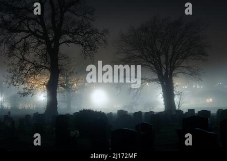 Ein gruseliges Konzept eines Friedhofs in einer nebligen Winternacht. Mit Gräbern, die von Straßenlaternen silhouettiert werden. Stockfoto