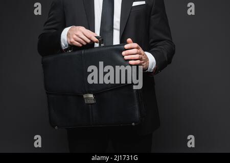 Verkürzte Ansicht eines Geschäftsmanns in Anzug mit Ledertasche auf dunkelgrau Stockfoto