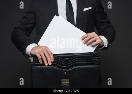 Abgeschnittene Ansicht des Geschäftsmannes, der Dokumente in einer Ledertasche auf dunkelgrau legt Stockfoto