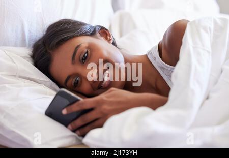 Er textete mir sofort zurück. Aufnahme einer jungen Frau, die ihr Handy benutzte, während sie in ihrem Bett lag. Stockfoto