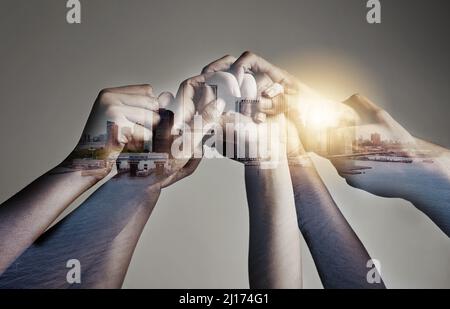 Unsere Einheit ist unsere Stärke. Aufnahme einer Stadt, die über einem nicht identifizierbaren Geschäftsteam mit Händen vor einem grauen Hintergrund übereinander liegt. Stockfoto