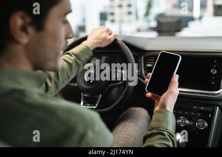 Nicht erkennbarer junger männlicher Fahrer, der sein Smartphone mit leerem Bildschirm in seinem neuen Auto hält, Mockup Stockfoto
