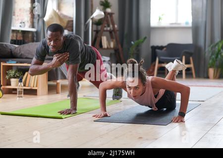 Sportlicher junger schwarzer Mann und kaukasische Frau, die Kräftigungsübungen im Wohnzimmer zu Hause machen Stockfoto