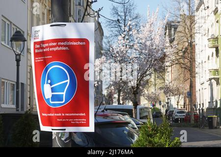 Bonn, Deutschland. 23. März 2022. In der Altstadt hängen Schilder mit der Aufschrift „Es wird empfohlen, eine medizinische Maske zu tragen“. Bald beginnt in Bonn die berühmte Kirschblüte. Die Stadt hat mit den Vorbereitungen für das Naturschauspiel begonnen und hat Schilder aufgehängt, die das Tragen einer Maske empfehlen. Im Jahr 2020 war die Altstadt während der Blütezeit wegen der Pandemie für Besucher komplett geschlossen. 2021 waren dort Masken Pflicht. Quelle: Oliver Berg/dpa/Alamy Live News Stockfoto