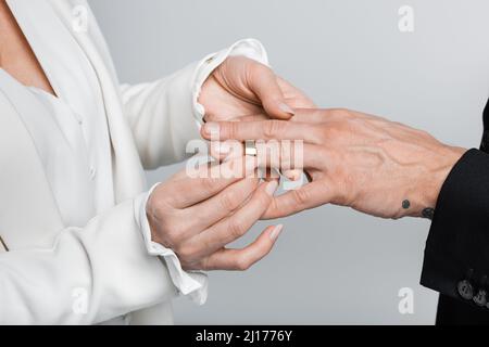 Verkürzte Ansicht einer reifen Frau, die einen Ehering auf dem Bräutigam trägt, isoliert auf Grau Stockfoto