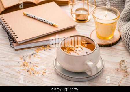 Heißer Kräutertee mit Notizblock, Kerze, Buch und Decke. Gemütlicher und hygge Lebensstil Stockfoto
