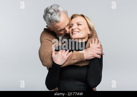 Grauhaariger Mann küsst und umarmt Frau isoliert auf grau Stockfoto