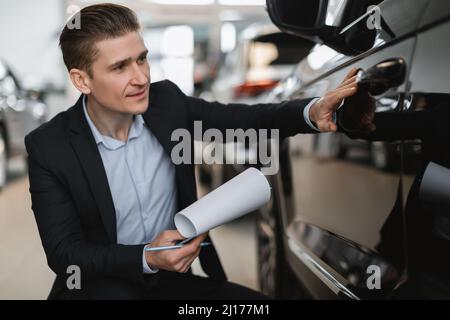 Gutaussehende Auto-Versicherung Agent sitzt in der Nähe von neuem Auto, so dass Check-up, Notizen an Autohaus-Center Stockfoto