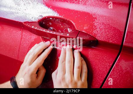 Hauptinstallation in der Risikozone unter den Griffen rotes Auto. Lackschutz ist Vinylfolie, Draufsicht. Stockfoto