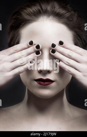 Sehen Sie kein Böses. Eine schöne blasse Frau mit dunklem Lippenstift, der ihre Augen bedeckt. Stockfoto