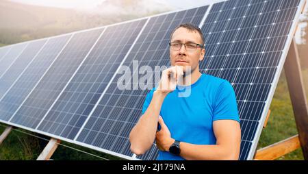 Portrait junger Bauer in Brille auf dem Hintergrund von Sonnenkollektoren. Das Konzept der Instandhaltung der elektrischen Elemente ist von selbst ausreichend. Stockfoto