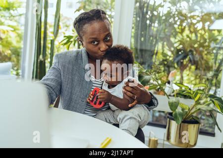 Geschäftsfrau küsst Sohn und arbeitet zu Hause am Laptop Stockfoto