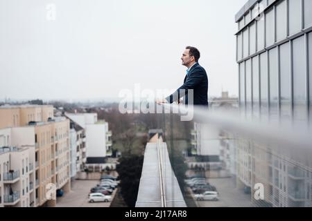 Nachdenklicher Geschäftsmann, der vor dem Gewächshaus am Geländer steht Stockfoto