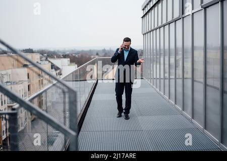 Glücklicher Geschäftsmann, der mit dem Handy spricht und auf dem Balkon läuft Stockfoto
