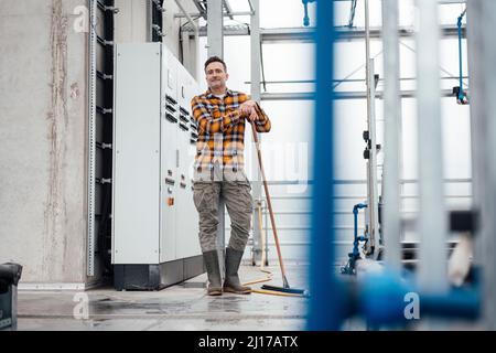 Mitarbeiter trägt Gummistiefel und steht mit Wischmopp im Gewächshaus Stockfoto