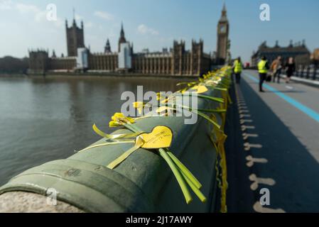 London, Großbritannien. 23. März 2022. Narzissen und gelbe Herzen, die an einem nationalen Tag der Reflexion von Familien auf der Westminster Bridge platziert wurden, die während der Pandemie von Covid-19 eine Liebesliebe verloren haben. Es ist der zweijährige Jahrestag der ersten Covid-19-Sperre. Bis heute hat das Vereinigte Königreich 186.094 Todesfälle verzeichnet, wobei Covid-19 auf der Sterbeurkunde erwähnt wurde. Kredit: Stephen Chung / Alamy Live Nachrichten Stockfoto