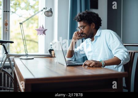 Mann mit Brille sitzt mit Laptop am Tisch Stockfoto