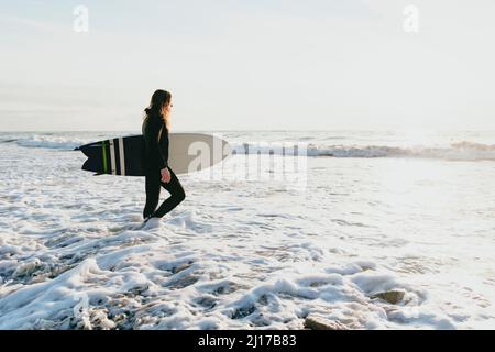 Surfer mit Surfbrett zu Fuß im Wasser am Strand Stockfoto