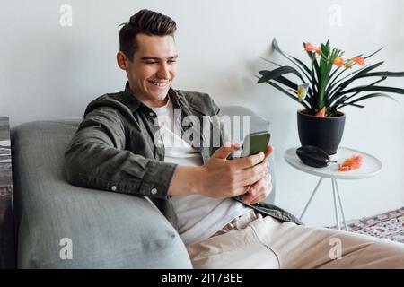 Glücklicher junger Mann, der zu Hause über das Mobiltelefon im Internet surft Stockfoto