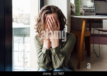 Depressive Frau, die zu Hause das Gesicht mit den Händen bedeckt Stockfoto