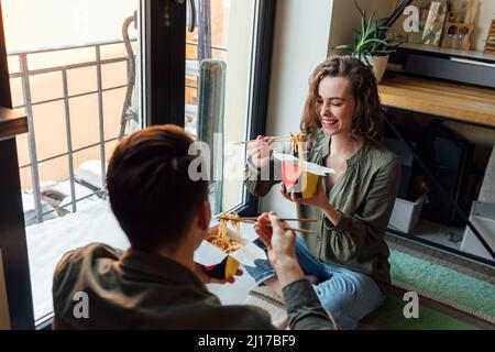 Fröhliche Frau, die mit ihrem Freund zu Hause Nudeln isst Stockfoto
