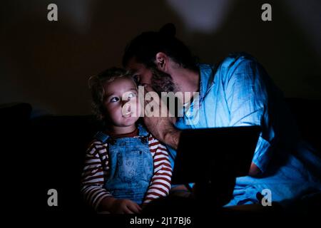 Vater mit Tablet-Computer, der zu Hause in das Ohr des Sohnes flüstert Stockfoto
