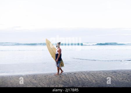 Mann, der Surfbrett trägt, läuft am Strand Stockfoto