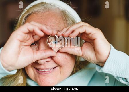 Lächelnde ältere Frau, die durch einen herzförmigen Ausstecher schaut Stockfoto