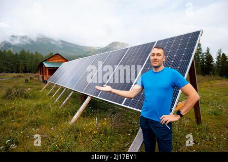 Der junge Mann lächelt und zeigt Sonnenkollektoren im Landhaus in den Bergen, das Leben in Island, Schweden, Finnland und Russland. Stockfoto