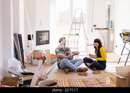 Junges Paar, das lachte und im Wohnzimmer Essen hatte Stockfoto