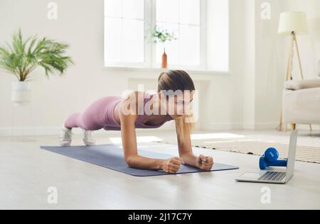 Sportliche Frau zu Hause bei sportlicher Planke beim Online-Video mit Fitnessübungen auf dem Laptop. Stockfoto