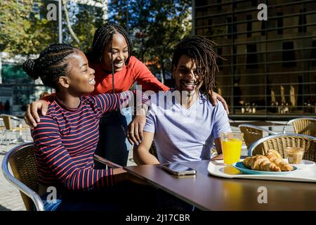 Lächelnde junge Frau, die sich mit Freunden im Straßencafé unterhielt Stockfoto
