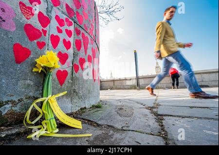 London, Großbritannien. 23. März 2022. Der zweite Jahrestag der ersten Absperrung – die Menschen besuchen immer noch die nationale Covid-Gedenkmauer vor dem St. Thomas' Hospital. Familie und Freunde von einigen der mehr als hundertachtzigtausend Menschen, die ihr Leben an Covid-19 verloren haben, haben mit der Hand Herzen an eine Wand gegenüber dem Parlament in London gezogen. Es wurde von den Covid-19 Hinterbliebenen Familien der Gerechtigkeit organisiert. Kredit: Guy Bell/Alamy Live Nachrichten Stockfoto