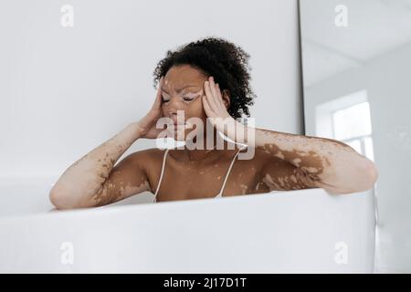 Frau, die zu Hause in der Badewanne sitzt und Kopfschmerzen hat Stockfoto