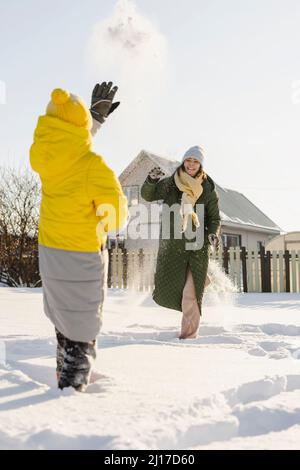 Frau wirft Schneeball auf Sohn stehen auf Tiefschnee im Winter Stockfoto