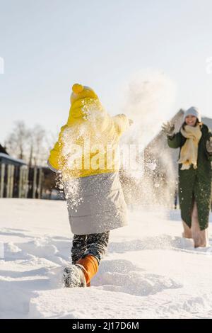 Fröhliche Mutter und Sohn, die sich im Winter Schnee auf einander werfen Stockfoto