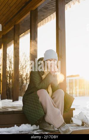 Frau, die auf der Veranda des Hauses im verschneiten Garten sitzt Stockfoto