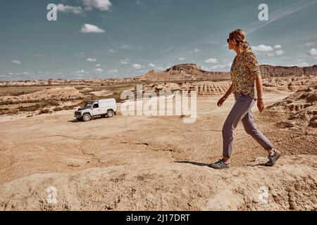 Frau, die das Auto beim Laufen in der Wüste, Bardenas Reales, Spanien, anschaut Stockfoto