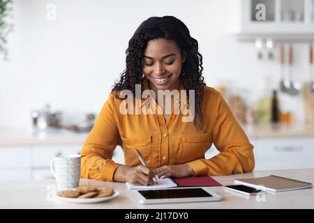 Positive schwarze Dame freiberuflich arbeitet von zu Hause aus, Notizen zu machen Stockfoto