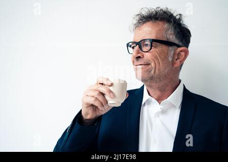 Lächelnder Geschäftsmann mit Kaffee vor weißem Hintergrund Stockfoto