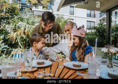 Glückliche Eltern, die mit Kindern auf der Geburtstagsparty im Hinterhof reden Stockfoto