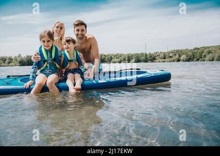 Lächelnde Familie mit Paddleboard am Wochenende im See Stockfoto