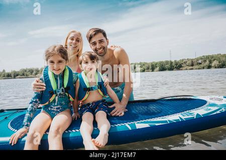 Kinder, die am Wochenende vor den Eltern auf dem Paddleboard sitzen Stockfoto