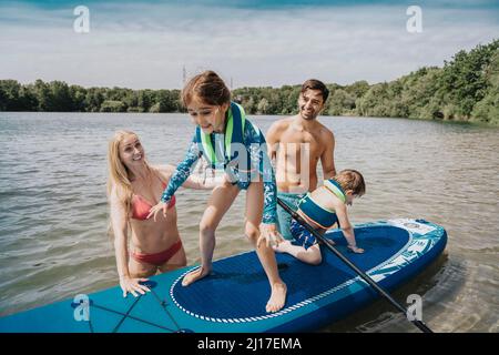 Geschwister auf dem Paddleboard, die von den Eltern über den See schweben Stockfoto