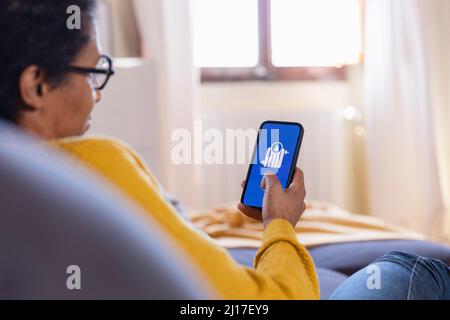 Frau, die die App für die Heimautomatisierung auf einem Smartphone im Wohnzimmer verwendet Stockfoto